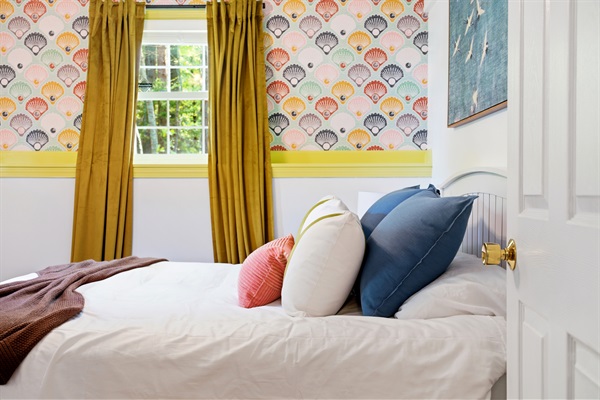 A charming bedroom featuring a comfortable bed set against elegant seashell-patterned wallpaper, creating a calm and coastal-inspired atmosphere.