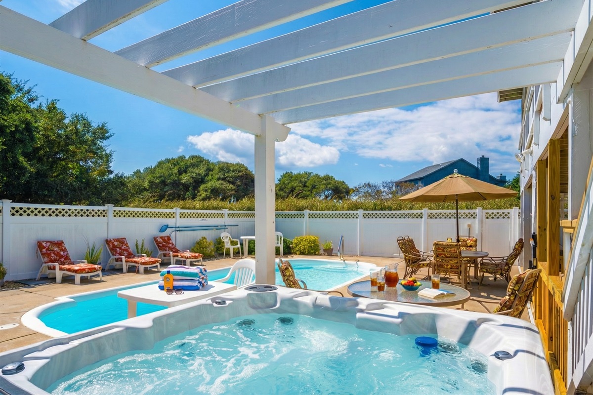 The relaxing poolside patio area complete with a bubbling hot tub, a white pergola for shade, and an outdoor table for al fresco dining.