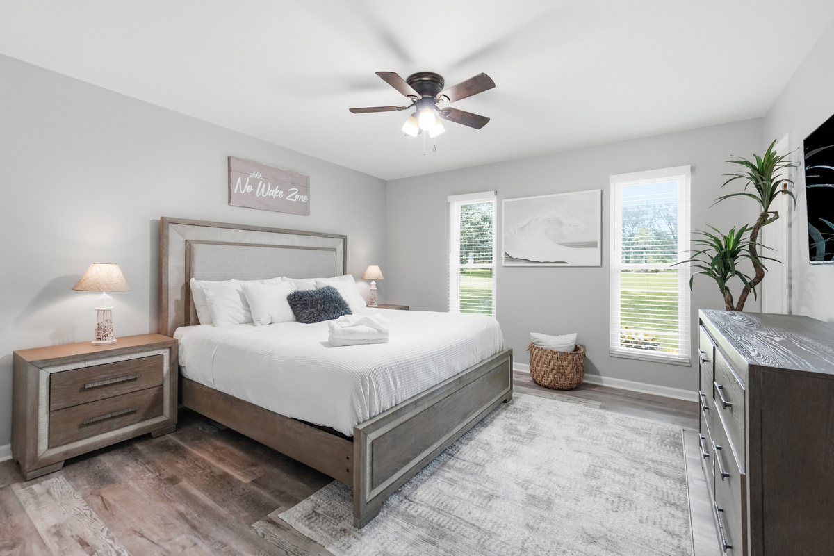 This spacious bedroom offers comfortable bedding, bedside lighting, a ceiling fan, and convenient storage.