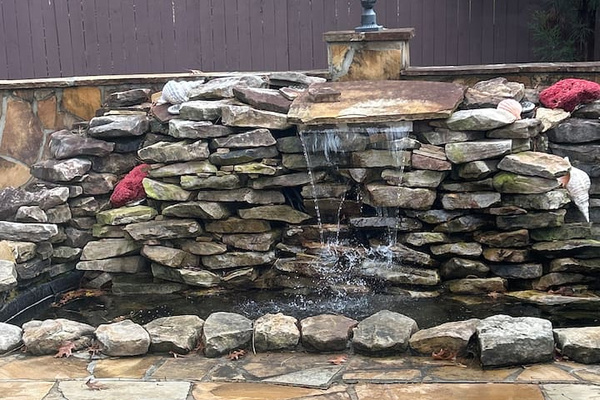 characters:

“Serene backyard pond with a natural stacked-stone waterfall, tranquil water feature, and flagstone patio. Surrounded by mature trees and privacy fencing, creating a peaceful retreat ideal for relaxation and outdoor entertaining.”