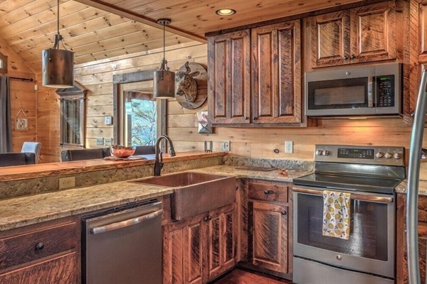 Fully equipped mountain kitchen with rustic wood cabinetry, stainless appliances, farmhouse sink and stone countertops - ready for family meals and group gatherings.