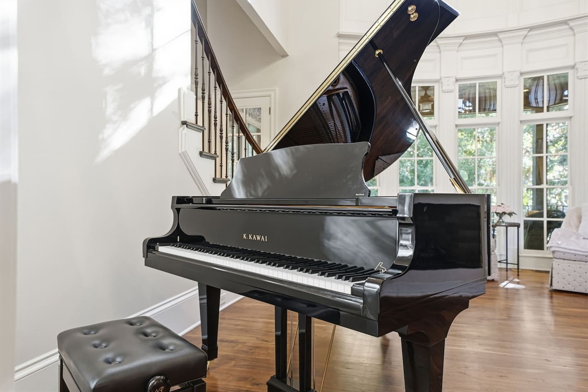 Beautiful entry sitting room with a grand piano, warm fireplace, tall windows, and two comfortable chairs. A bright, serene spot to unwind or enjoy quiet moments.