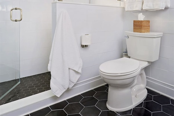 The spacious second-floor ensuite bathroom features sleek hexagon tile floors and a large shower with high-end polished nickel Kohler fixtures, including a convenient handheld, all enclosed in custom frameless glass for a modern, sophisticated look.