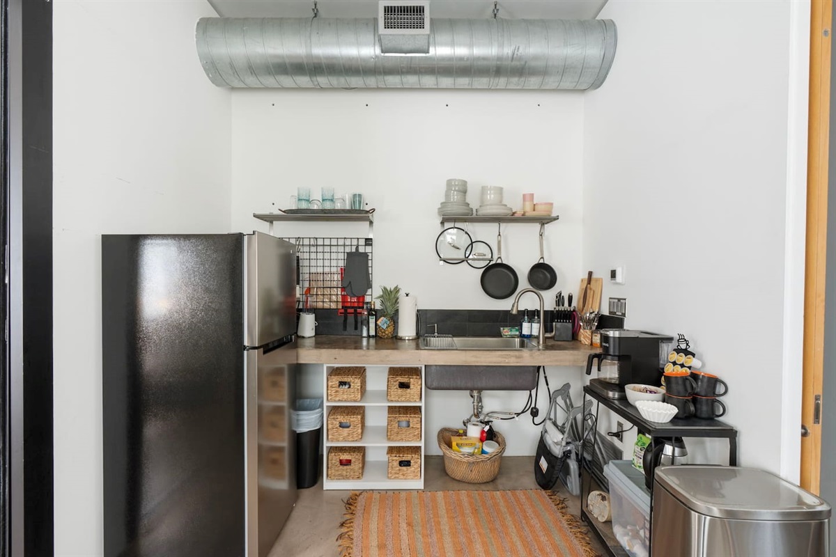 Compact modern kitchenette with open shelving, stainless steel appliances, and industrial-style accents.
