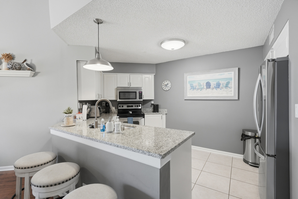 The fully equipped kitchen features stone countertops, solid wood cabinets, and modern appliances, including a refrigerator, range/oven, microwave, dishwasher, and garbage disposal. Everything you need to prepare meals.