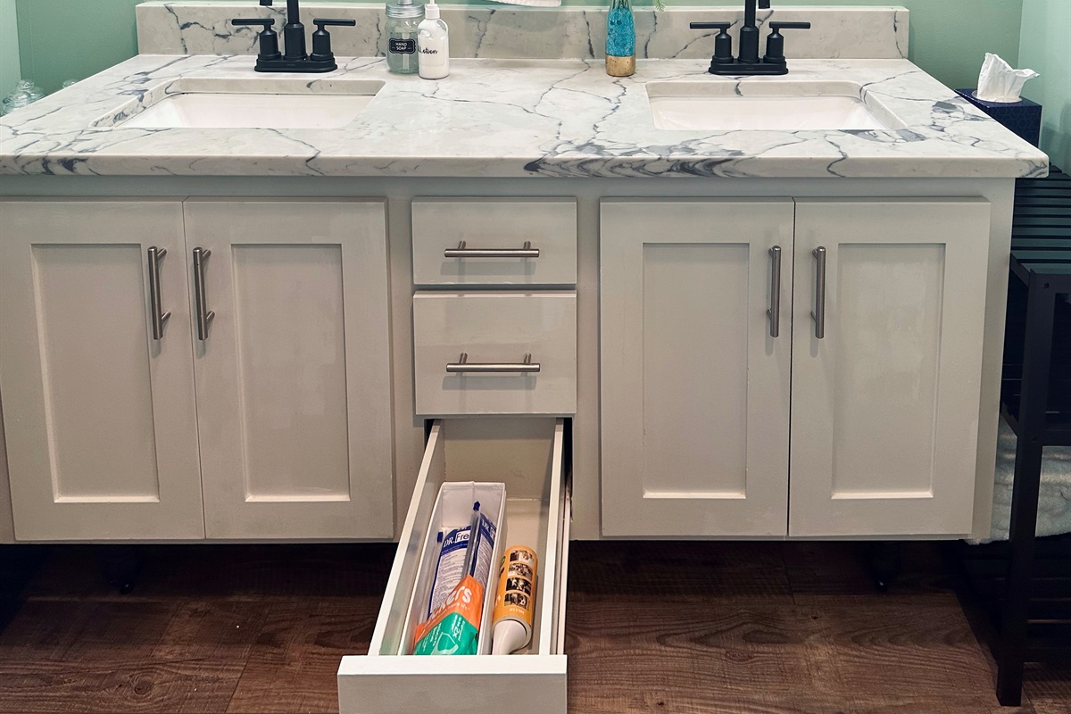 Ensuite vanity drawer organized with toothbrushes, toothpaste, floss, and a lint roller for practical everyday needs.