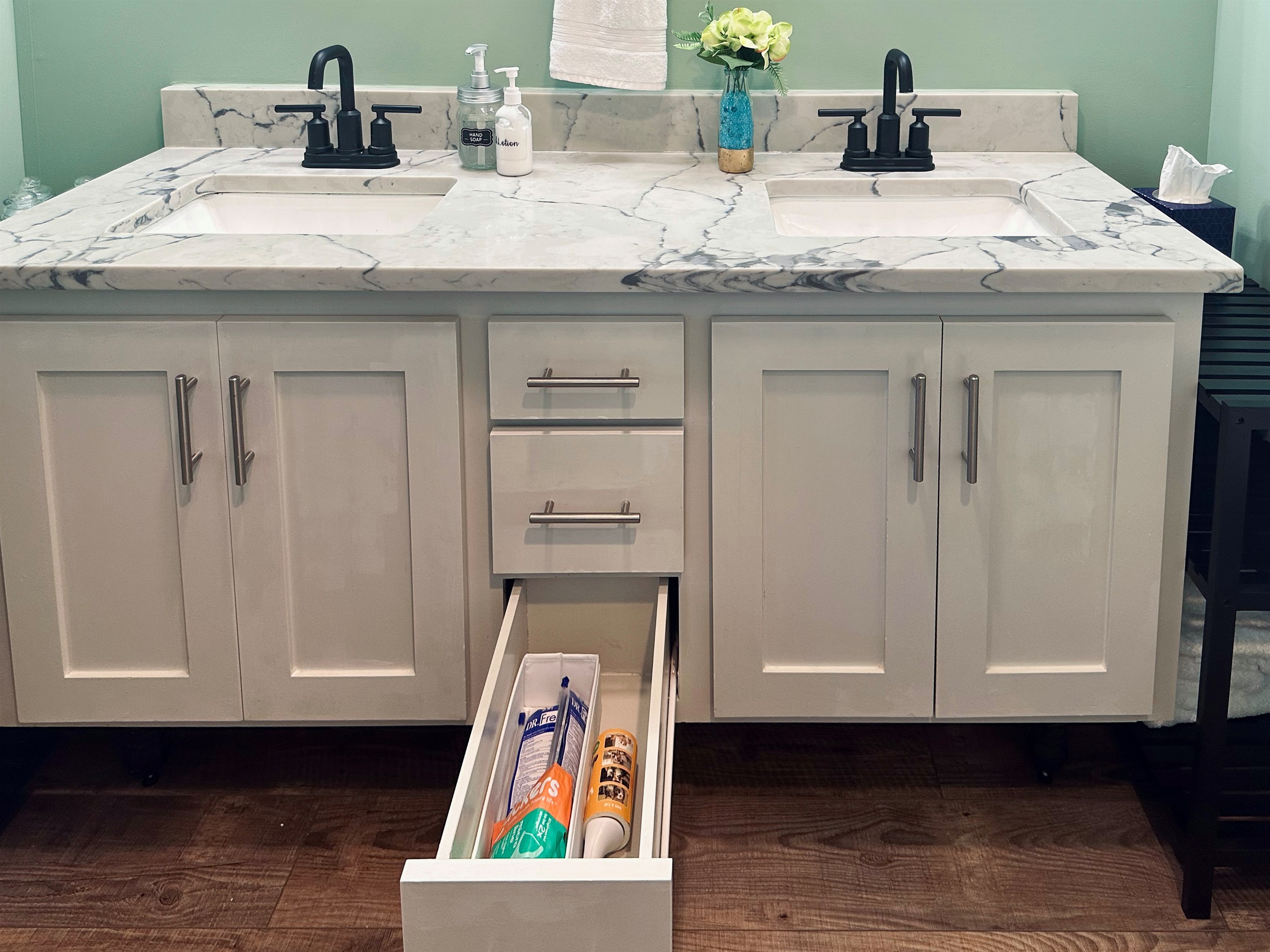 Ensuite vanity drawer organized with toothbrushes, toothpaste, floss, and a lint roller for practical everyday needs.