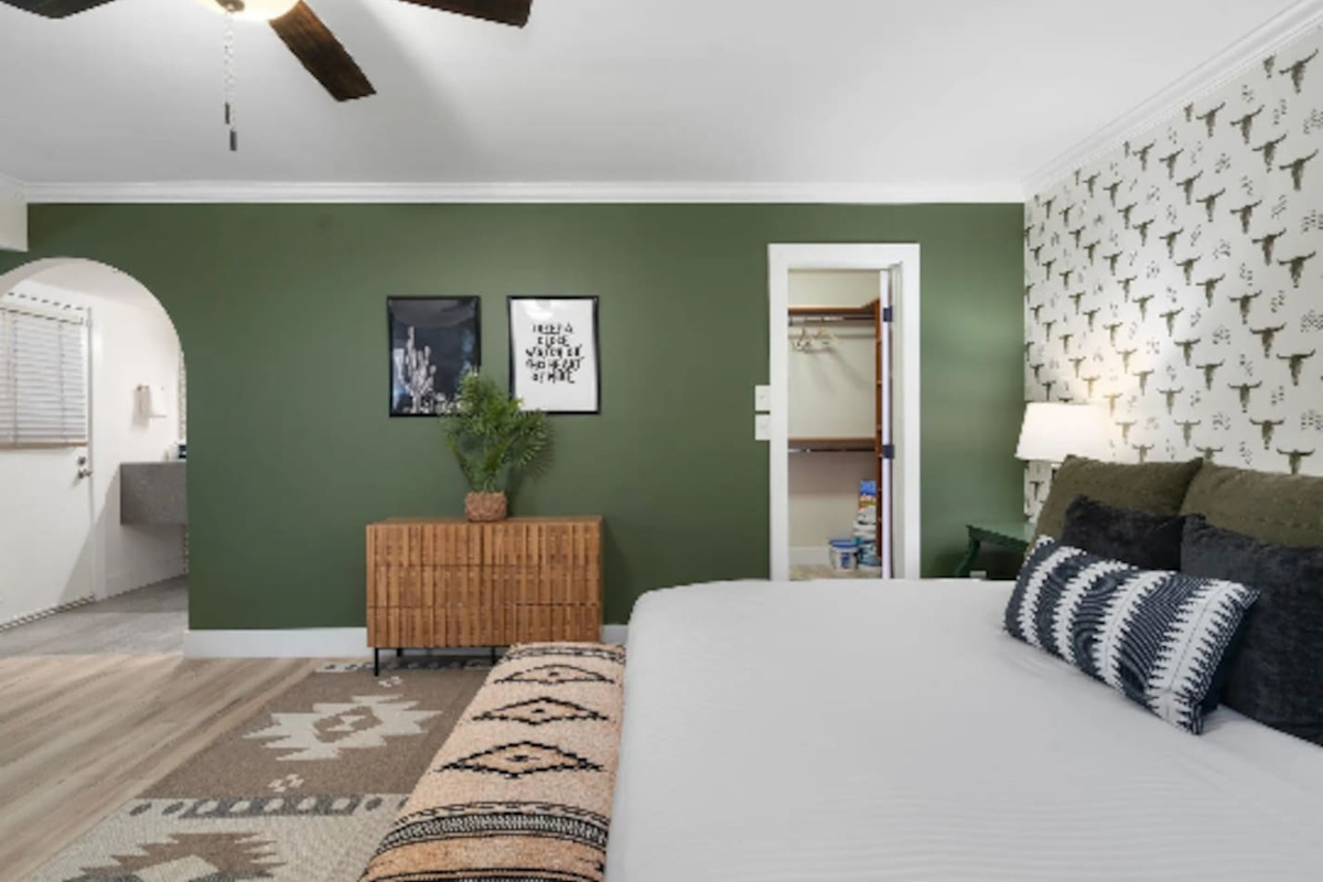 Tucked behind the bed, a walk-in closet and private bath keep this room feeling like its own suite. The olive green wall and framed prints add just enough personality without overwhelming the space.