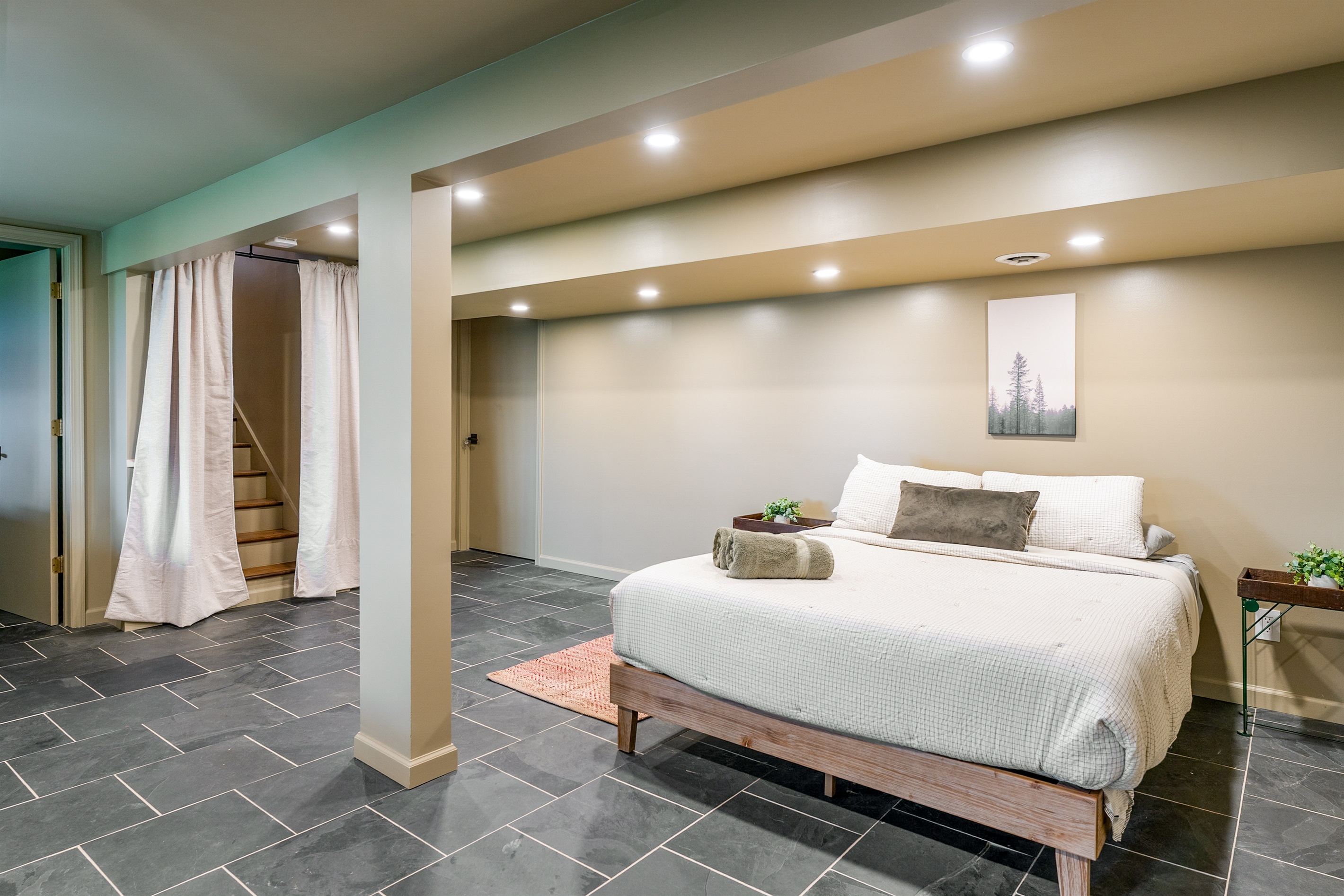 Spacious lower-level queen bedroom with cozy lighting, slate floors, and a clean modern vibe for restful nights.