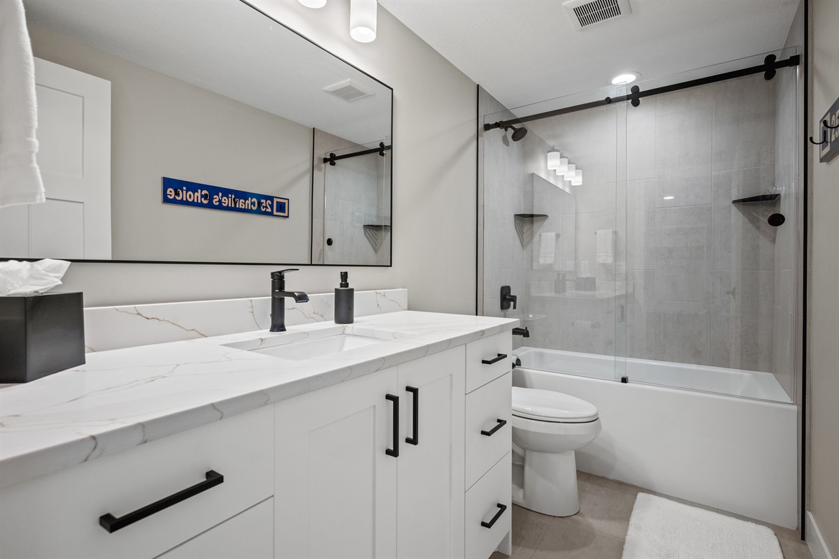 Large quartz countertop, expansive mirror, and a tub-shower combo with sleek glass doors—perfect for unwinding after a day of adventure.