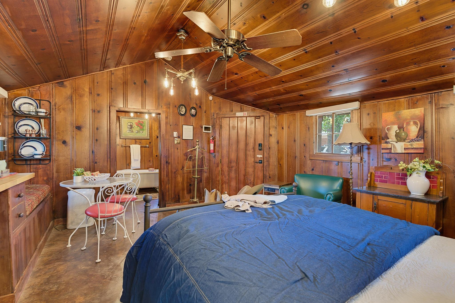 Papaw's Cabin cozy log cabin bedroom featuring vaulted wood-paneled ceiling, bistro dining table, clawfoot tub view, and vintage decor. Unique Waco, Texas getaway.