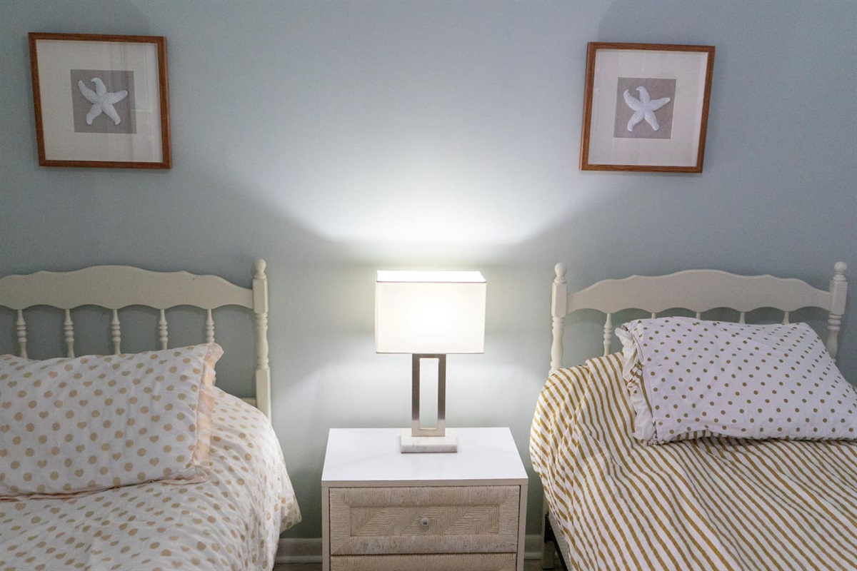 Cozy coastal twin bedroom featuring soft beachy tones, charming starfish artwork, and warm ambient lighting — the perfect retreat after a day in the sand and sun.