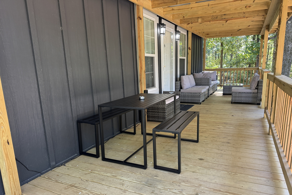 Large covered porch with sectional sofa, coffee table, and dining set, perfect for relaxing in the woods