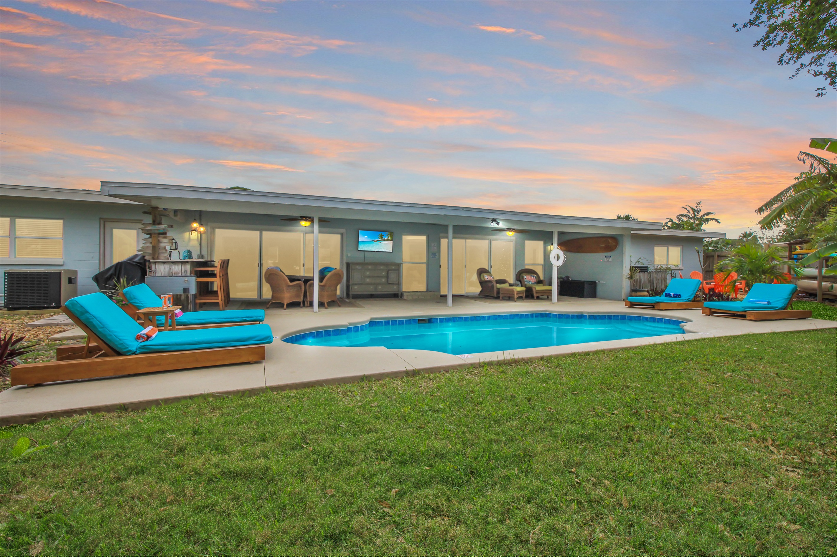 Large, private backyard features a heated pool with loungers and large covered patio with TV, bar, dining, and outdoor living room areas.  Also, there's a fire pit, hammock, and tree swing