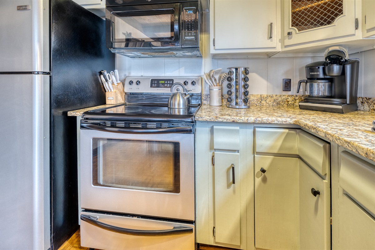 The kitchen features a stainless steel stove, microwave, refrigerator, Keurig coffee maker, and spacious countertop. Bright and inviting with natural light.