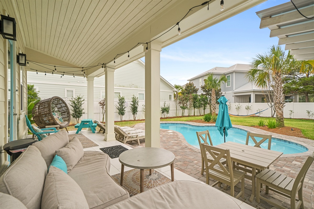 Covered back patio with comfortable seating and views of the pool and yard.
