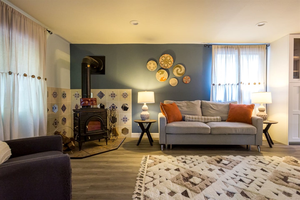 - Lounge with stylish sofa, armchair, and vibrant throw pillows for color
- Classic wood stove with decorative tile detail brings warmth & timeless character
- Layered lighting design enhances both ambiance and relaxation throughout the space