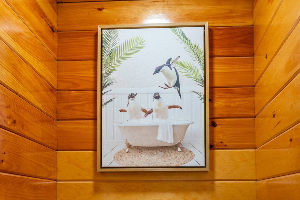 Enjoy the playful, whimsical charm added by this framed penguin bathtub art print. Mounted securely over the toilet alcove area, this fun piece complements the warm wood paneling while showcasing the home’s thoughtful design touches.