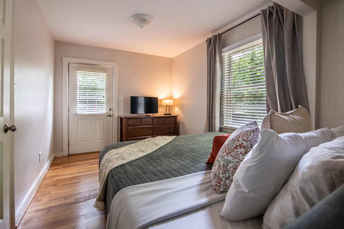 Charming queen bedroom with dresser, TV, and windows that fill the space with light.