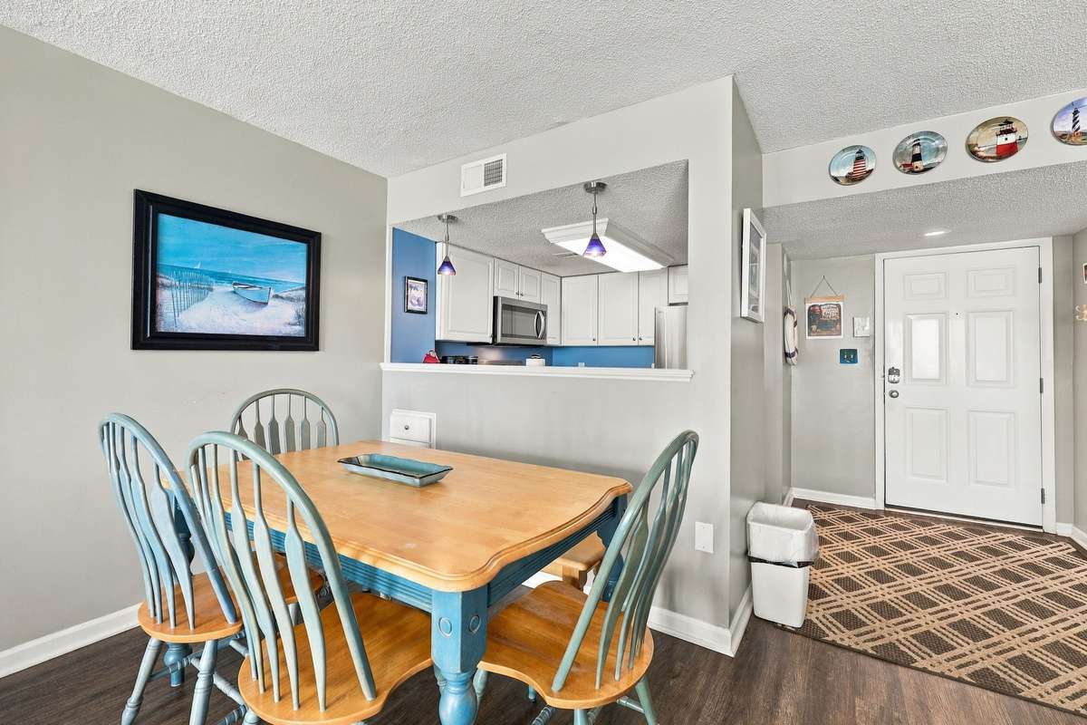 Dining area view showcasing a wooden dining table with blue-accented chairs, opening up to the main entryway and kitchen pass-through.
