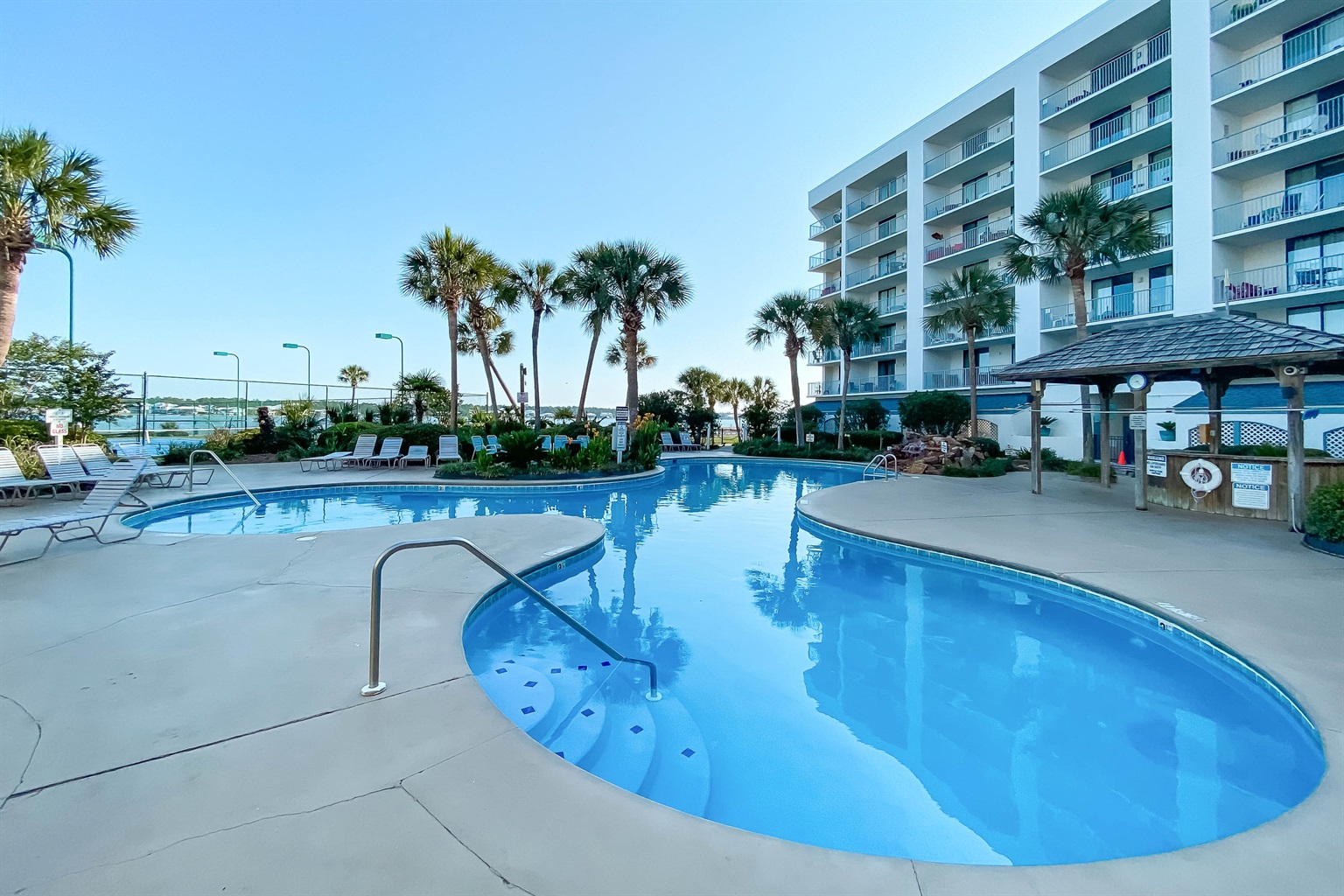 A tranquil waterside escape awaits. This inviting pool and patio area, complete with comfortable loungers and dining tables, offers the perfect spot to relax and soak in stunning views of the bay.