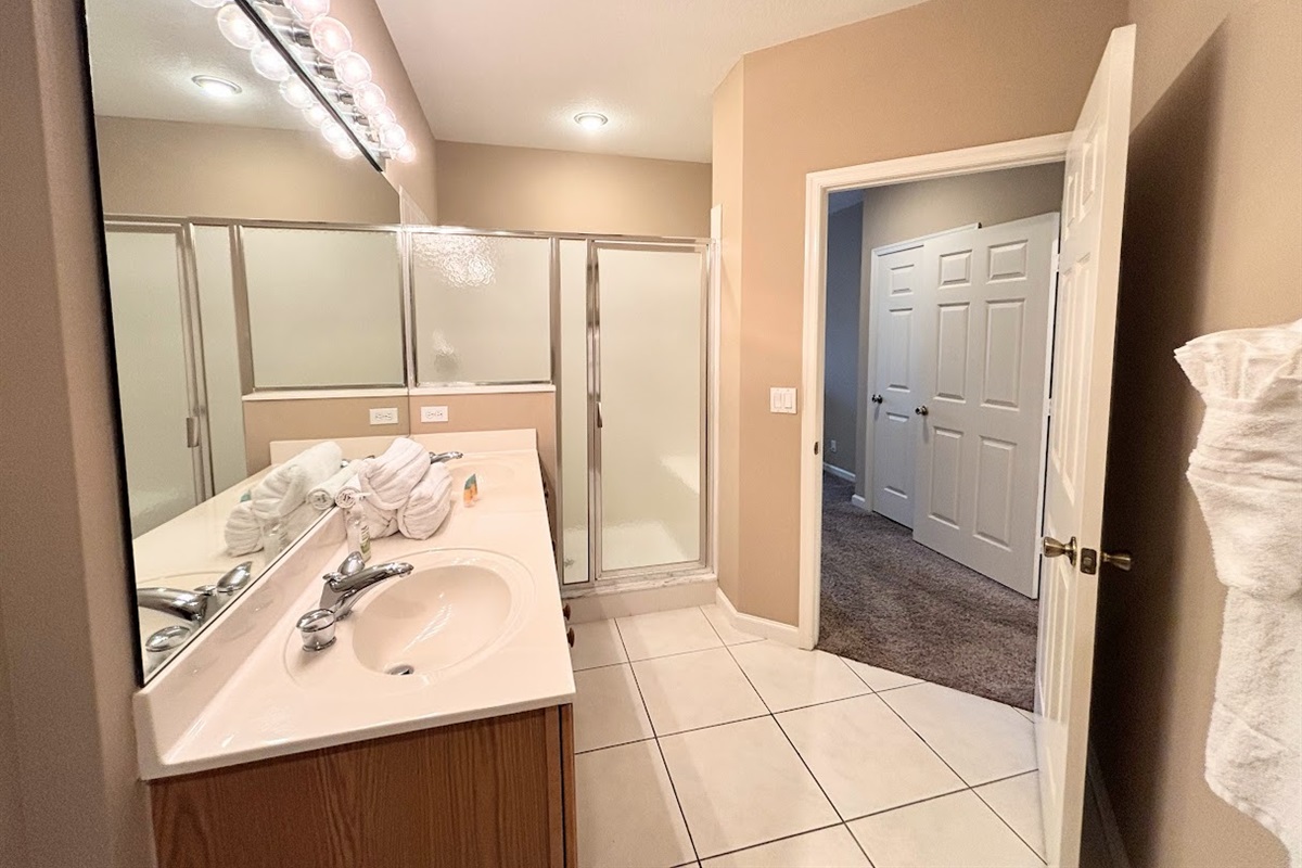 Bright bathroom featuring a large vanity, full mirror, tile flooring, and a walk-in shower with glass doors.