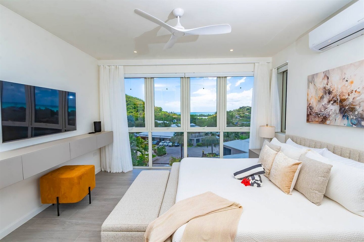 Master bedroom with king size bed, en-suite bathroom, air conditioning, ceiling fan, wall mounted tv, closet and gorgeous views of the ocean and hillside.