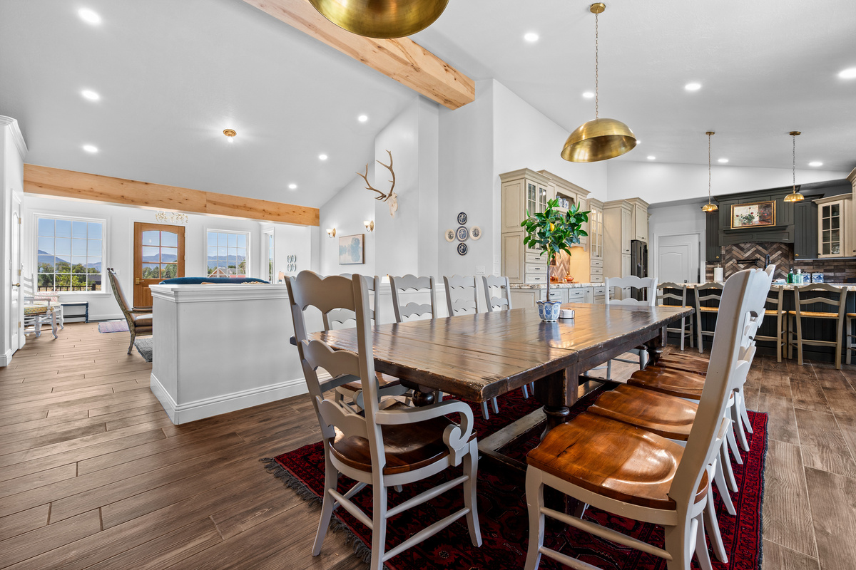 The expansive dining area is designed for memorable gatherings, featuring a substantial farmhouse table, generous seating, warm wood flooring, and an effortless connection to the kitchen and living spaces.