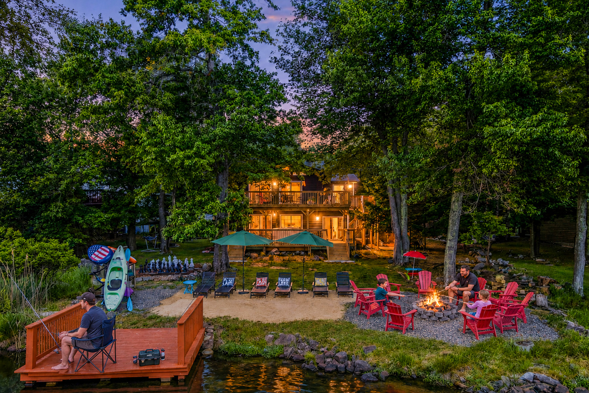  Élevé Lake Lodge at dusk — warm evening light bathes the lakefront yard, dock, and fire pit seating on Lake Carobeth