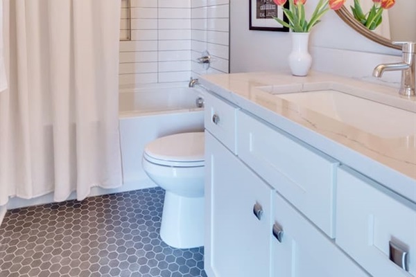 - Subway tiled shower and tub combo behind a soft white curtain for a clean, classic look - Bright vanity with quartz counter & chrome fixtures offers style & functionality - Pops of color from fresh tulips and hex tile floor add personality and warmth