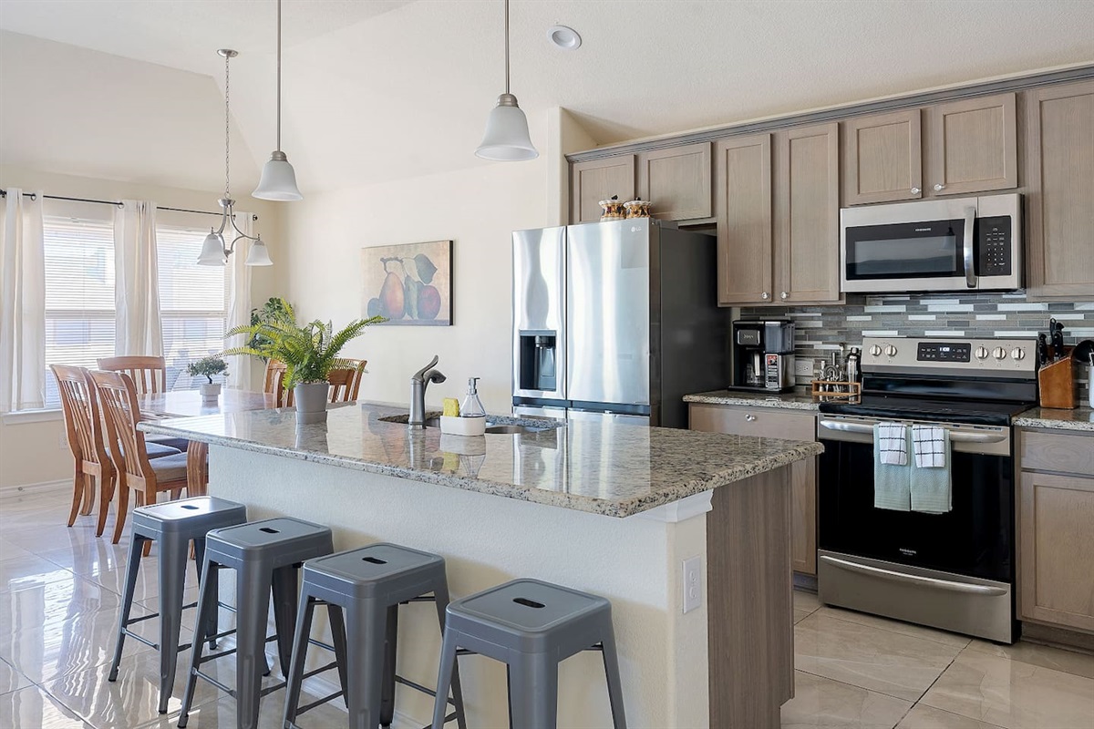 Step into this modern kitchen featuring stainless steel appliances, a sleek granite countertop island with bar stools, and contemporary pendant lighting.