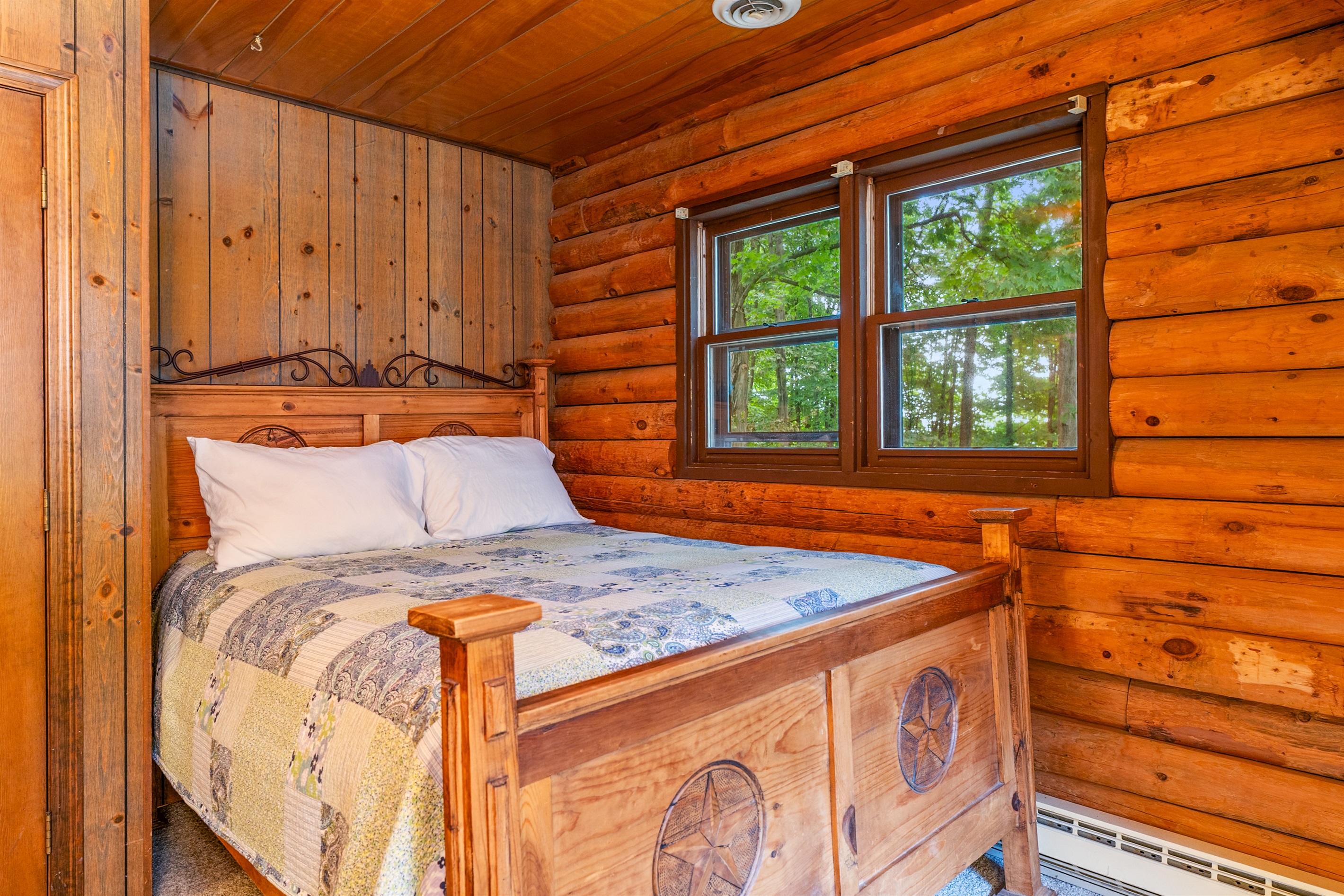 Bedroom #2 Charming log cabin bedroom with a queen bed and twin bed, natural wood beams, and bright windows showcasing forest views.