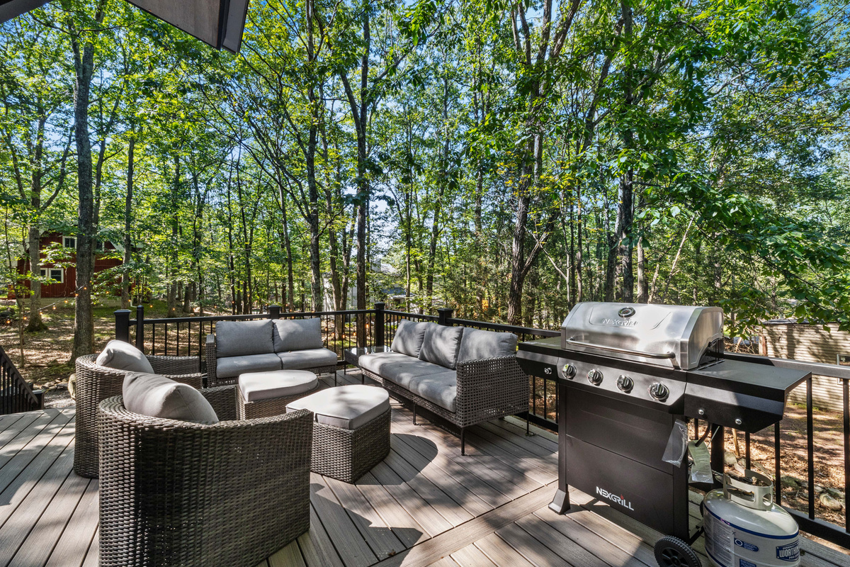 A private outdoor deck with dining space and a stone fire pit set against a wooded backdrop