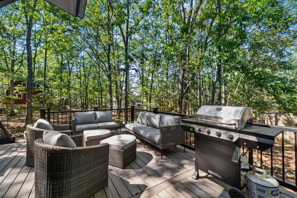 A private outdoor deck with dining space and a stone fire pit set against a wooded backdrop