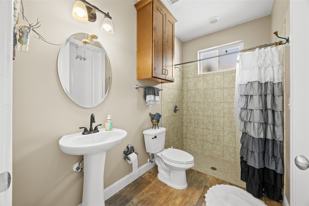 Bright bathroom with pedestal sink, round mirror, and ruffled shower curtain in Jacksonville Beach rental home.