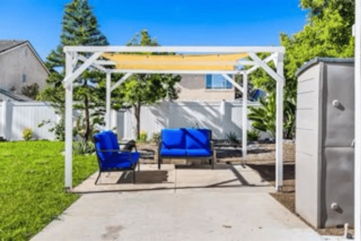 Covered patio area with seating for 4 witha  BBQ grill (propane) nearby and outdoor furniture, perfect for outdoor dining and relaxing evenings.