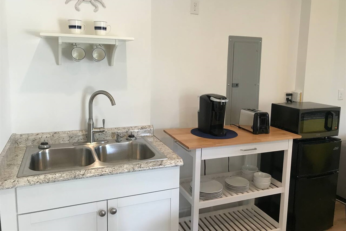 Kitchenette with stocked Keurig, toaster, microwave, refrigerator, freezer, dishes and silverware.