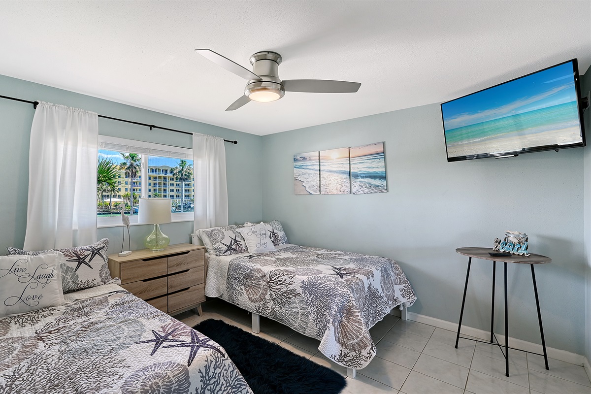 Guest bedroom has two full-size beds and TV plus view of the boat docks and inlet