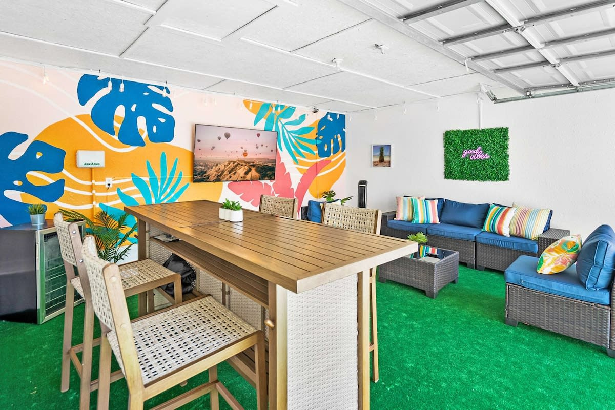 Lift the garage door and the tiki lounge opens straight onto the pool deck: painted mural, bar stools, sofas on green turf and a big smart TV. This is where your group will end up every single evening of the week.