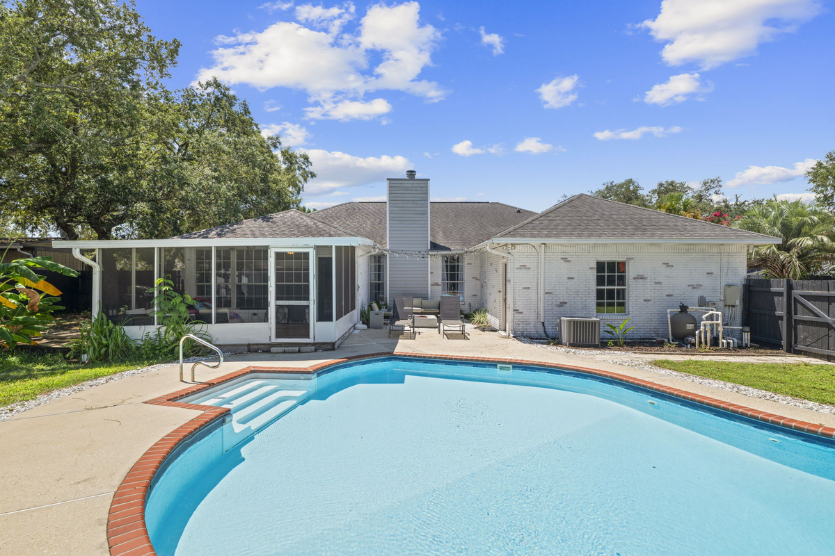 The whole backyard oasis — pool, patio, and covered porch — all set against the classic white-brick home.