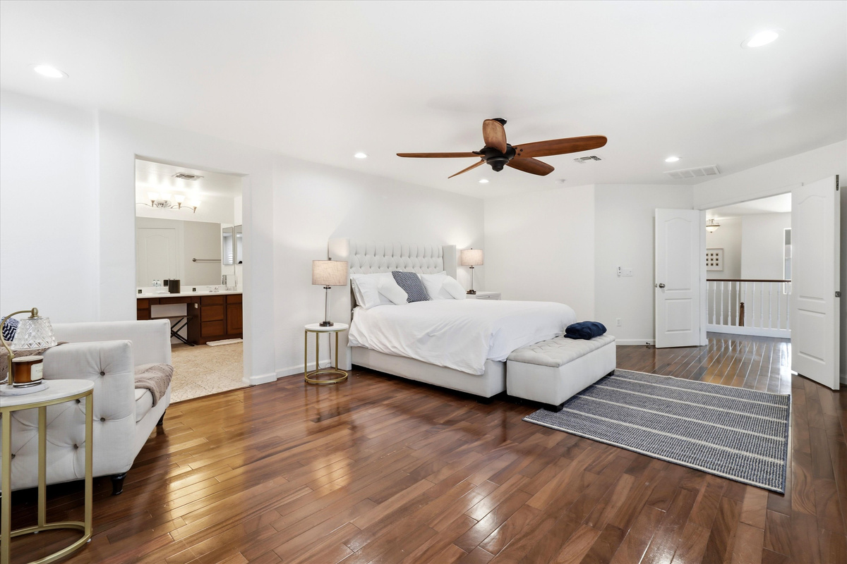 Primary bedroom with a large bed, sitting chair, wood floors, and easy access to the ensuite bathroom.