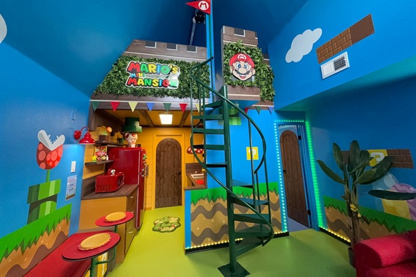 Discover the whimsical lower level of Mario's Mini Mansion in Clermont, FL! Green spiral staircase leads to the castle fort with 'Mario's Mini Mansion' sign, red stools, and colorful Super Mario decor throughout. Fun space with kitchenette access.