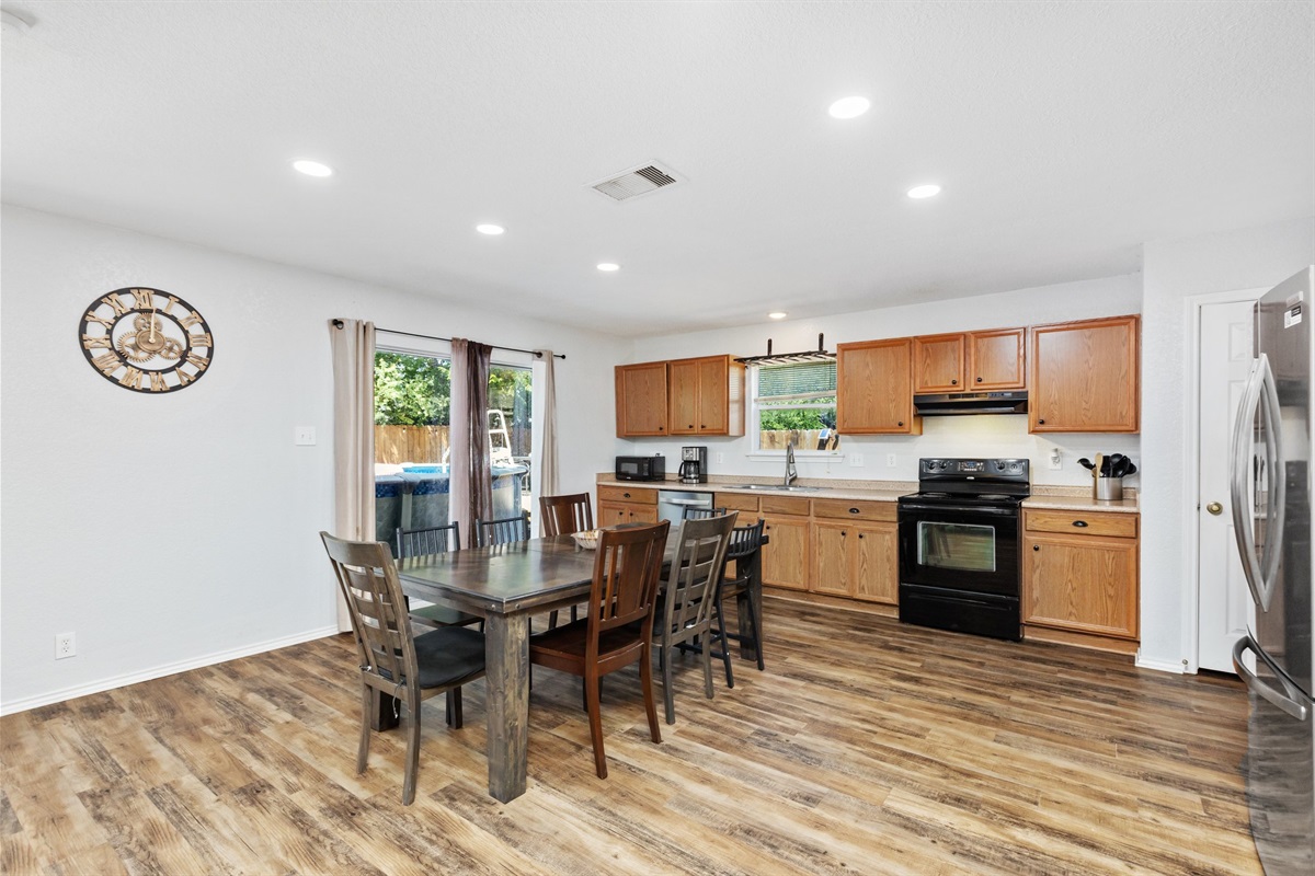 Full kitchen with stainless refrigerator, wood cabinetry, and dining table for group meals. Open main floor layout keeps everyone connected — great for extended stays and long-term guests in San Antonio.