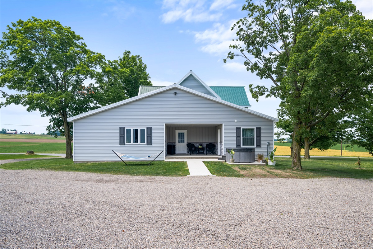 Spacious rear view with a covered patio, hot tub, and wide open farmland perfect for relaxing evenings