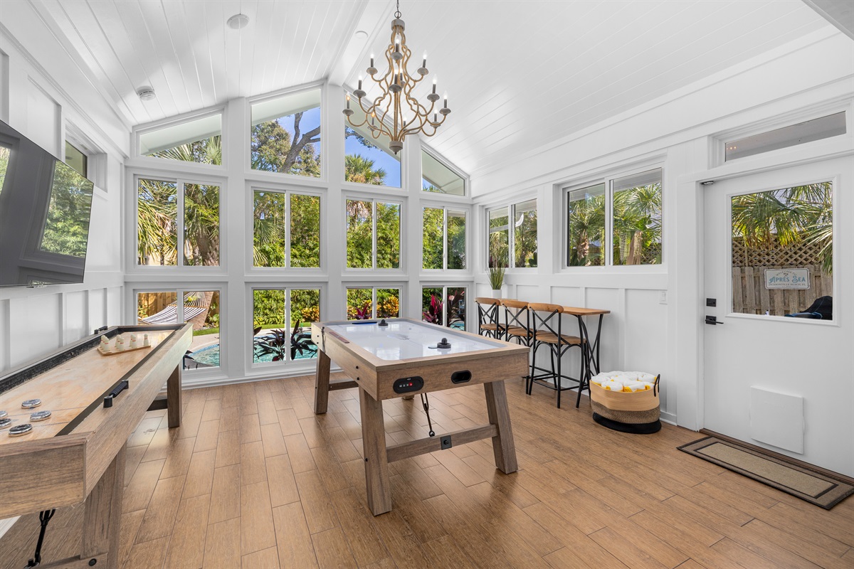Bright game room with floor to ceiling windows, featuring both shuffleboard and foosball - perfect for family fun and rainy-day entertainment