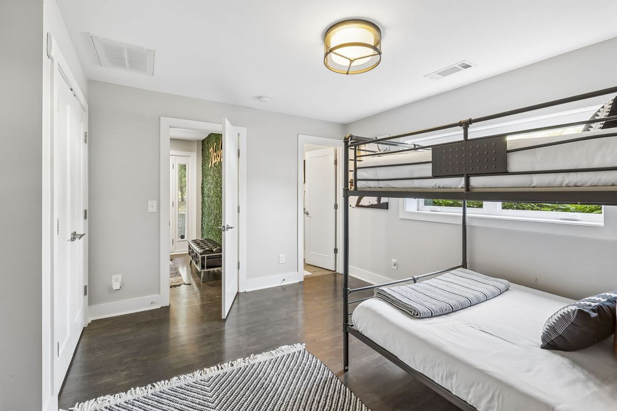 Stylish queen over queen bunk bed, dressed in modern striped linens - Includes a sleek desk, wall mounted TV, and tall mirror for comfort and convenience - Monochrome rug and minimalist d&eacute;cor create a polished, cozy sleep and work space