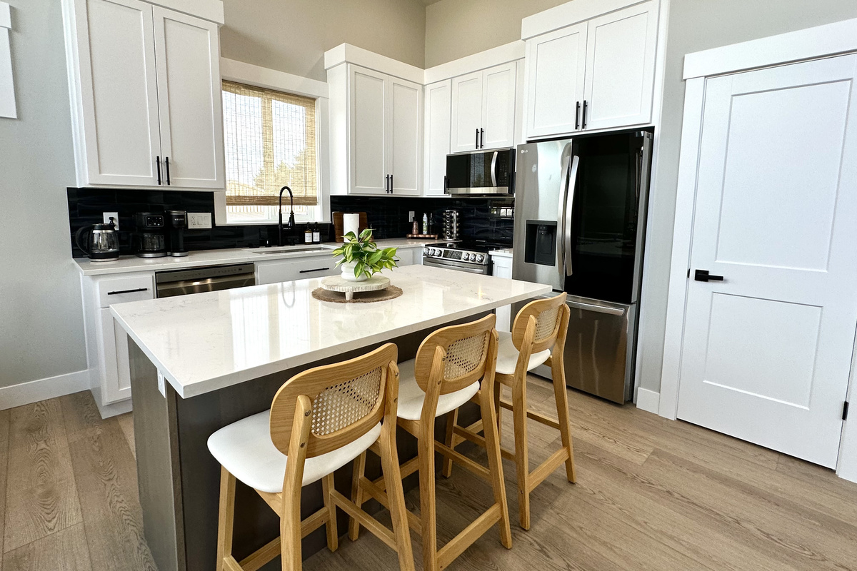 The kitchen sits just off the great room — white quartz counters, full-size stainless appliances and island seating for three. Bring your clothes and your groceries; we have the rest.