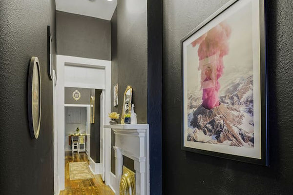 Stroll through this epic hallway with original wood floors, bold art, an exploding pink volcano, and a gold fireplace.