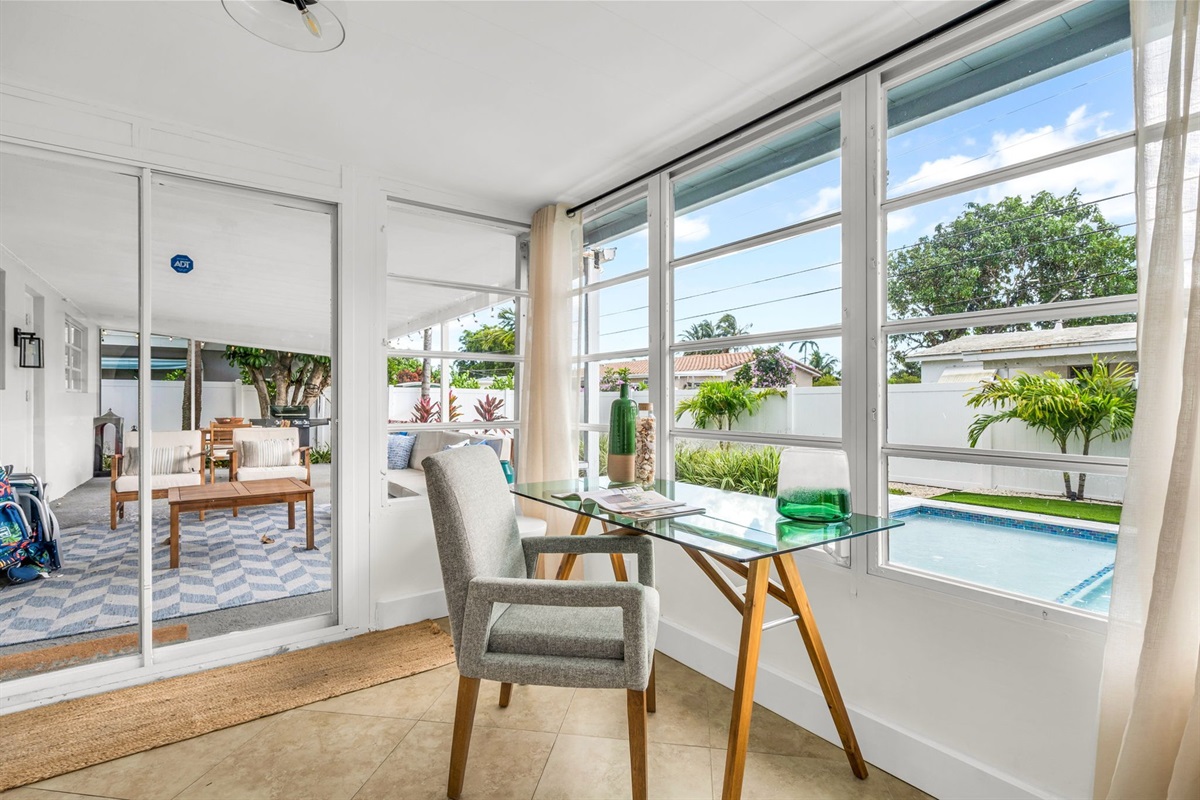 A beautifully designed Florida sunroom with wrap-around windows, modern furnishings, a Smart Fire streaming TV, and tranquil pool views—ideal for lounging, morning coffee, or working in style.