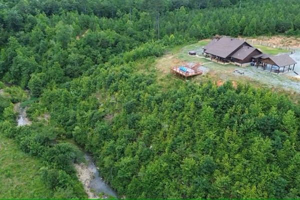 Aerial perspective of the cabin surrounded by forest and open land.